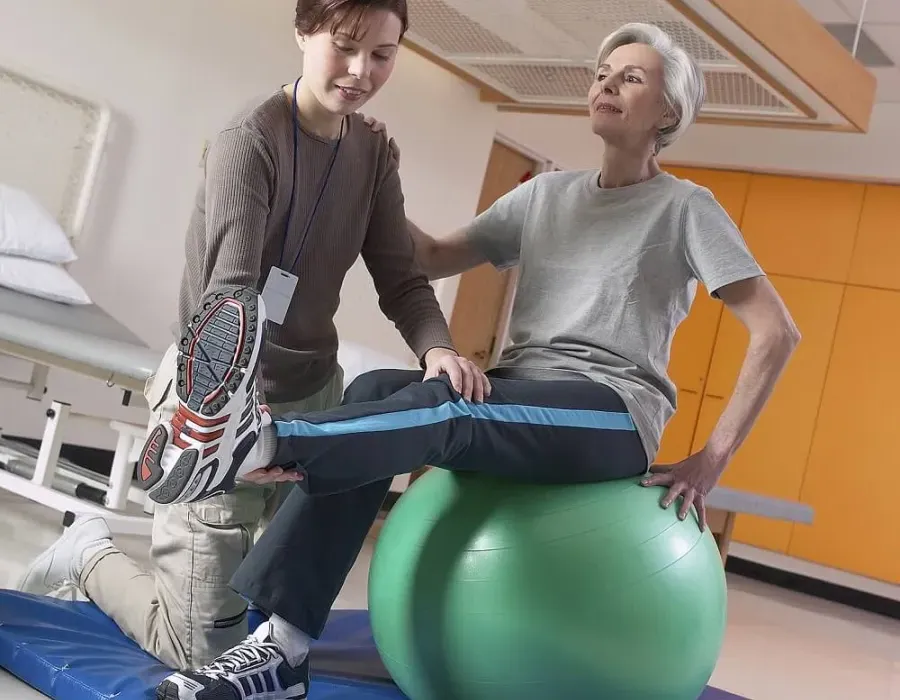 Physical therapist assistant providing PTA services for patient stretching on exercise ball